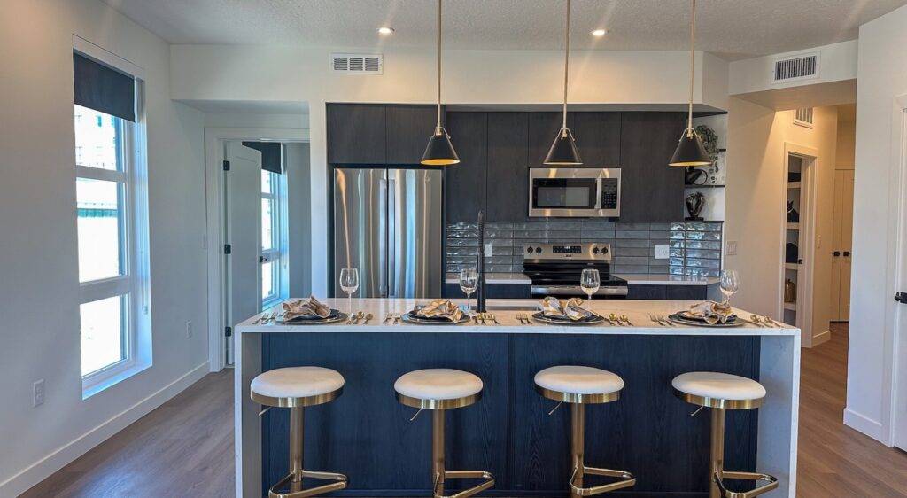 Modern kitchen with navy island, gold bar stools, marble counter, pendant lights, stainless steel appliances, and elegant table setting for four.