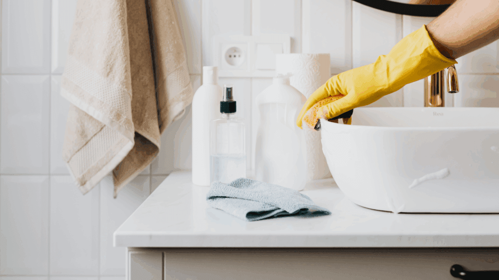 A person wearing yellow gloves cleans a sink, representing the cleaning services of SCS Multifamily.
